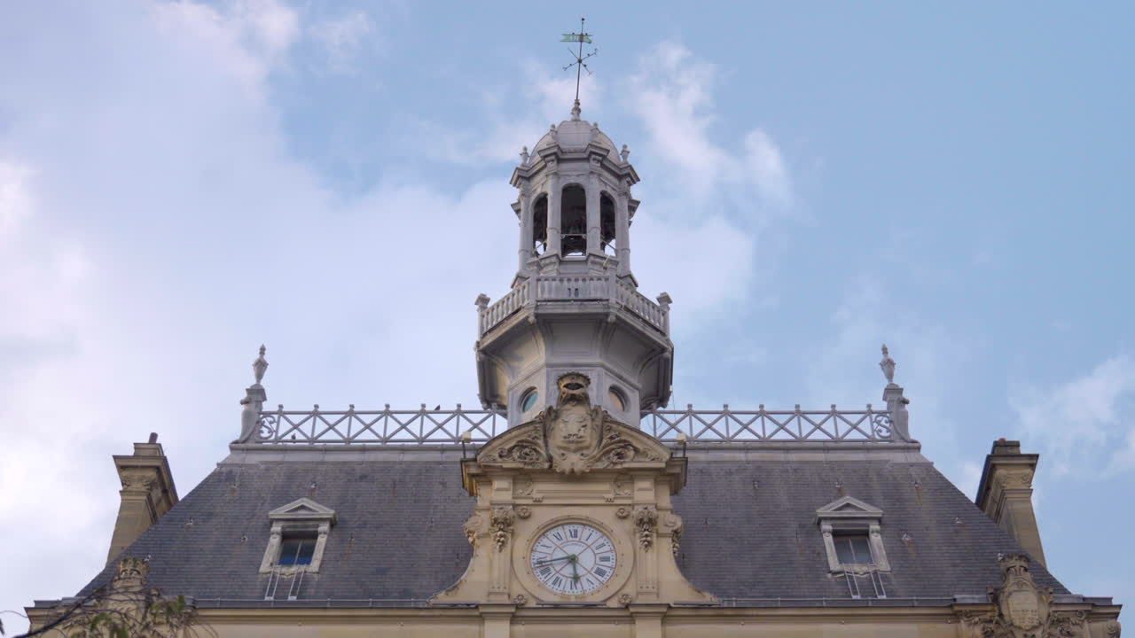 A close-up shot of the roof of the Hôtel de Ville in Asnières-sur-Seine, focusing on its 19th-century clock and tower with a decorative weather vane under clear daylight