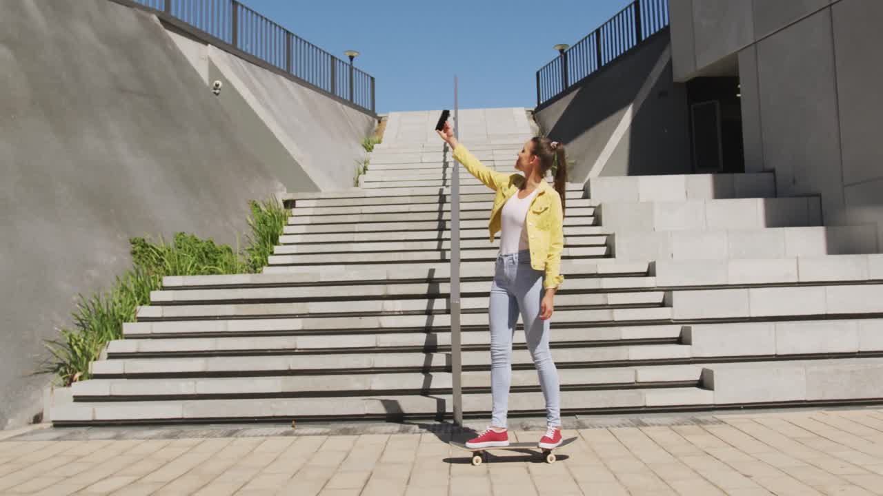 Smiling caucasian woman skateboarding, taking selfie on sunny day