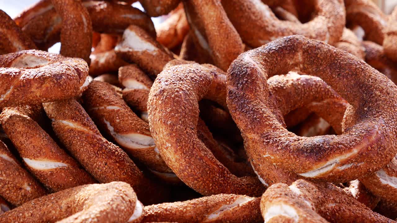 A close-up view of a pile of traditional Turkish simit, with a hand reaching in to pick one