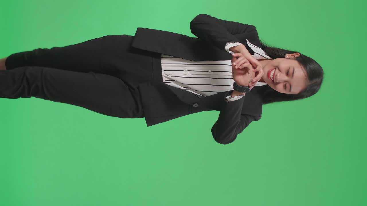 A Smiling Asian Business Woman Looking At A Watch While Walking Through Green Screen In The Studio