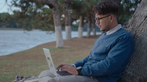 man using laptop by tree in park