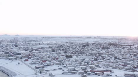 Puesta-De-Sol-En-El-Pueblo-Cubierto-De-Nieve-De-Reykjanesbær-En-Islandia,-Antena