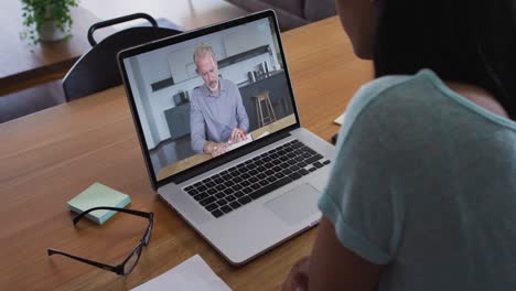 Mixed-race-businesswoman-sitting-at-desk-using-laptop-having-video-call-with-male-colleague