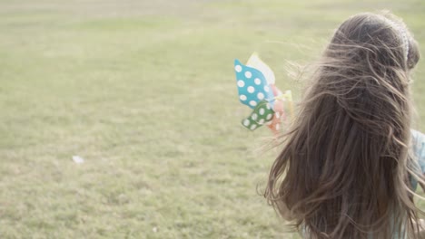 vista posteriore della bambina che corre sul prato con ventaglio di carta