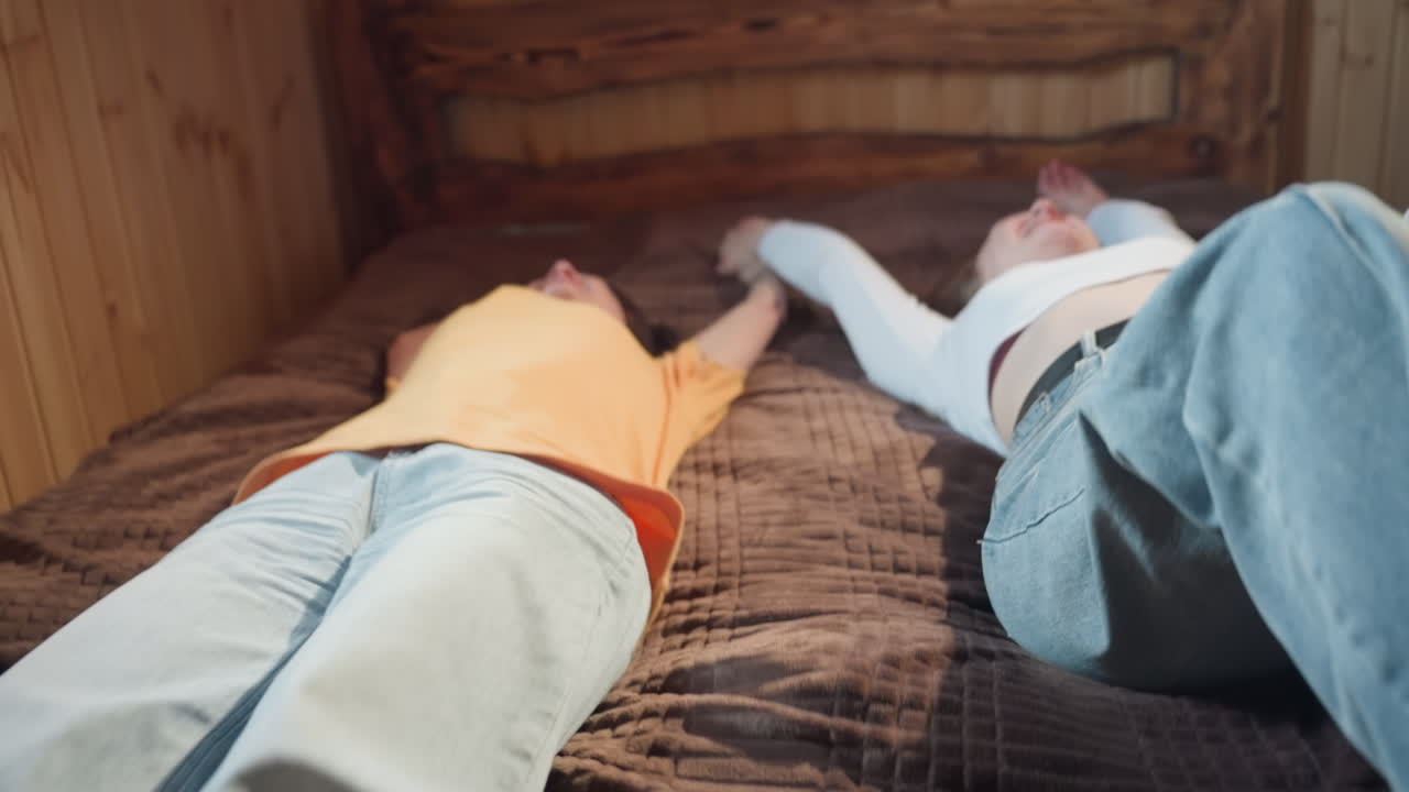 middle aged woman with gentle smile looks at daughter in cozy wooden room as they fall back to bed, sunlight filtering through window