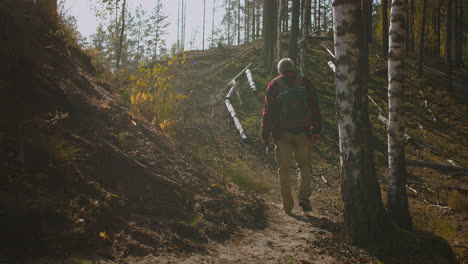 Ruhiger-Spaziergang-Des-Fischers-Im-Wald-Am-Sonnigen-Morgen.-Ein-Mann-Mit-Angelrute-Und-Rucksack-Geht-Langsam-Zwischen-Bäumen-Hindurch