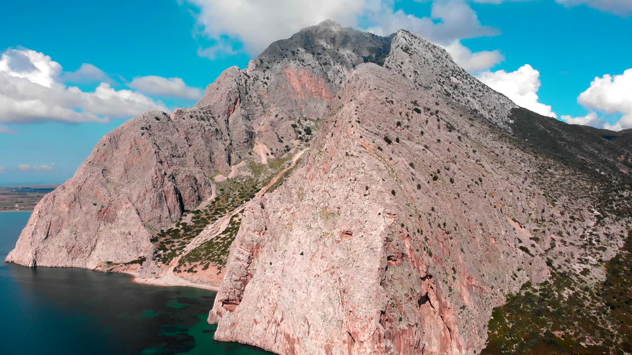 Tall Mountain Surrounded By Deep Blue Sea Under White Clouds On Blue Sky In Greece - DJI Drone Shot