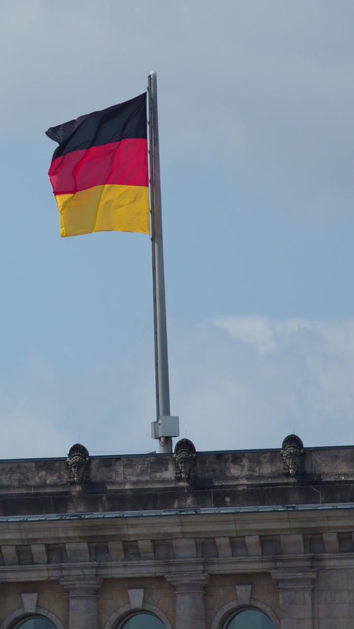 Bendera Jerman berkibar di atas arsitektur bersejarah di bawah langit berawan, kamera statis, cahaya siang alami, Berlin.