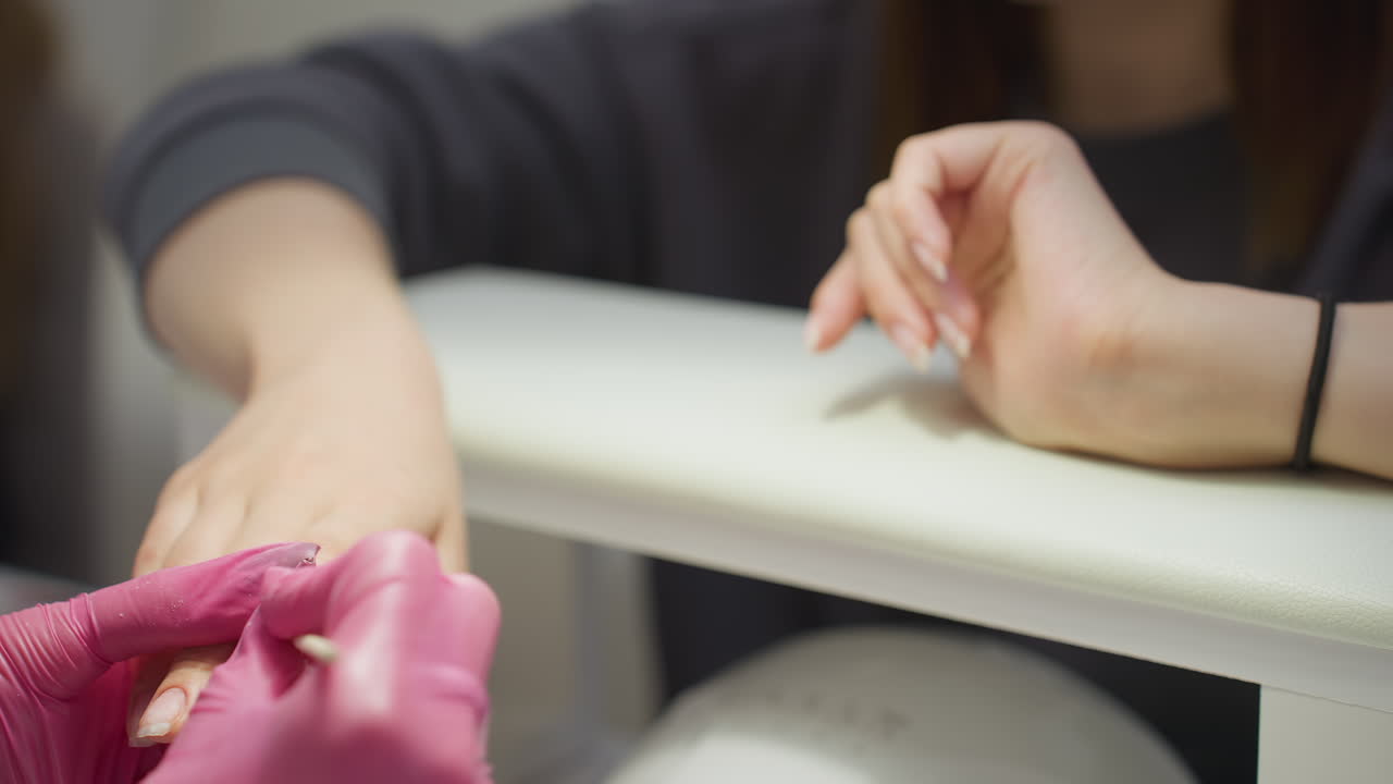 Closeup view of customer hands with natural nails resting on support cushion above UV nail dryer in preparation for final steps of manicure process inside bright, clean, and modern nail salon setting