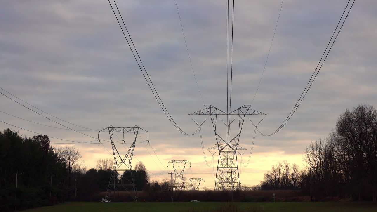 Long shot of electrical transmission towers stretching into the distance against somber cloudy sky at sunset