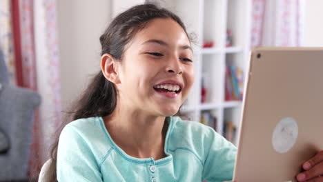 young girl sitting at desk in bedroom playing with digital tablet