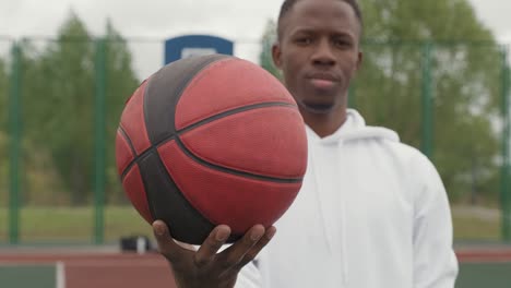 young smiling active male basket player in gray sweatshirt holding ball while standing on playground 1