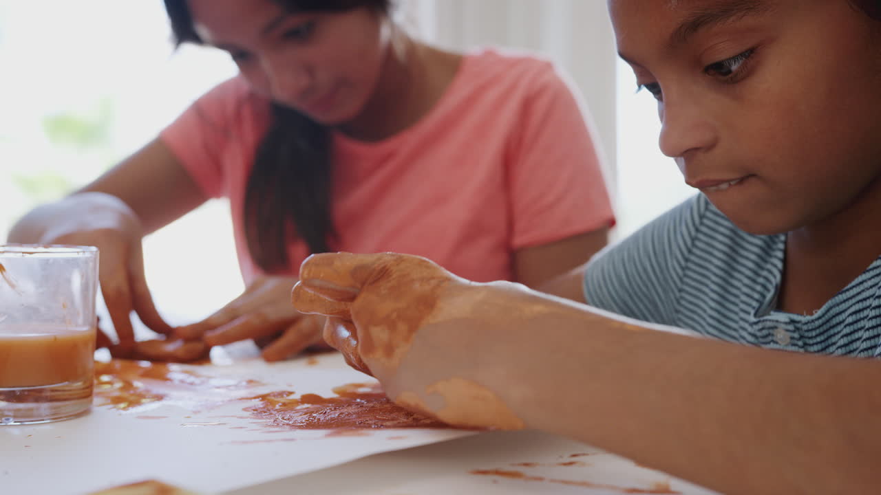 Close up of two pre-teen girls&rsquo; dirty hands playing with modelling clay at home, mid section