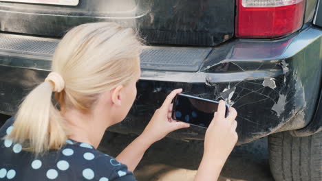 a woman photographs a damaged car bumper