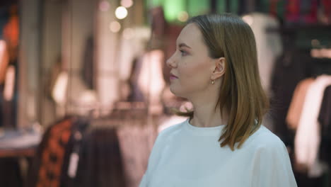 young lady in white top thoughtfully gazing at clothing store display, surrounded by warm lighting and vibrant colors with mannequins in background