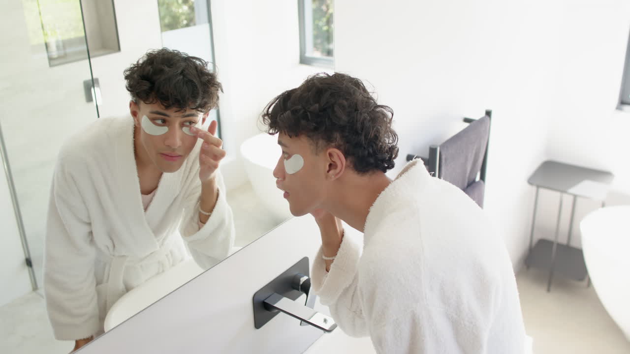 Applying under-eye patches, person in bathrobe looking in bathroom mirror