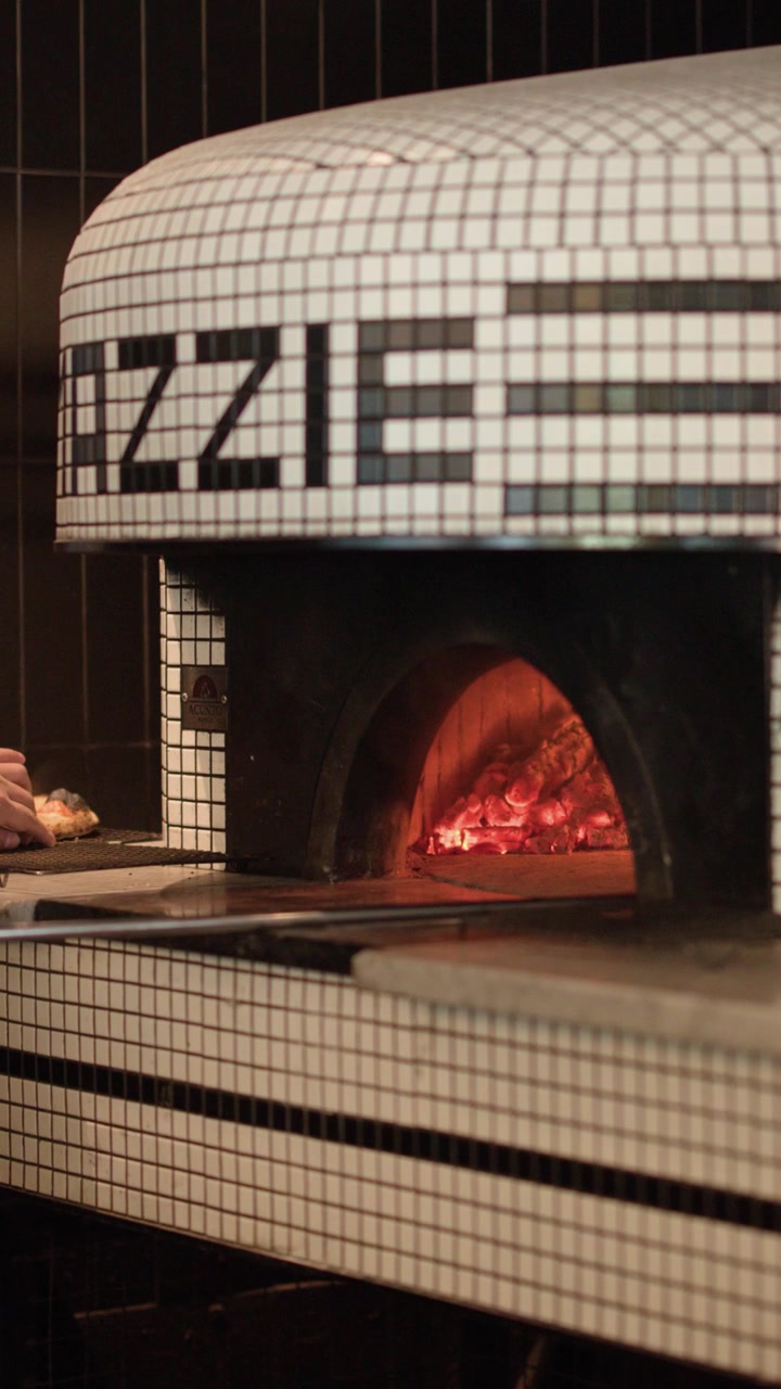 Primo piano di uno chef che gira la pizza all'interno di un forno a legna incandescente a Bangkok, Thailandia