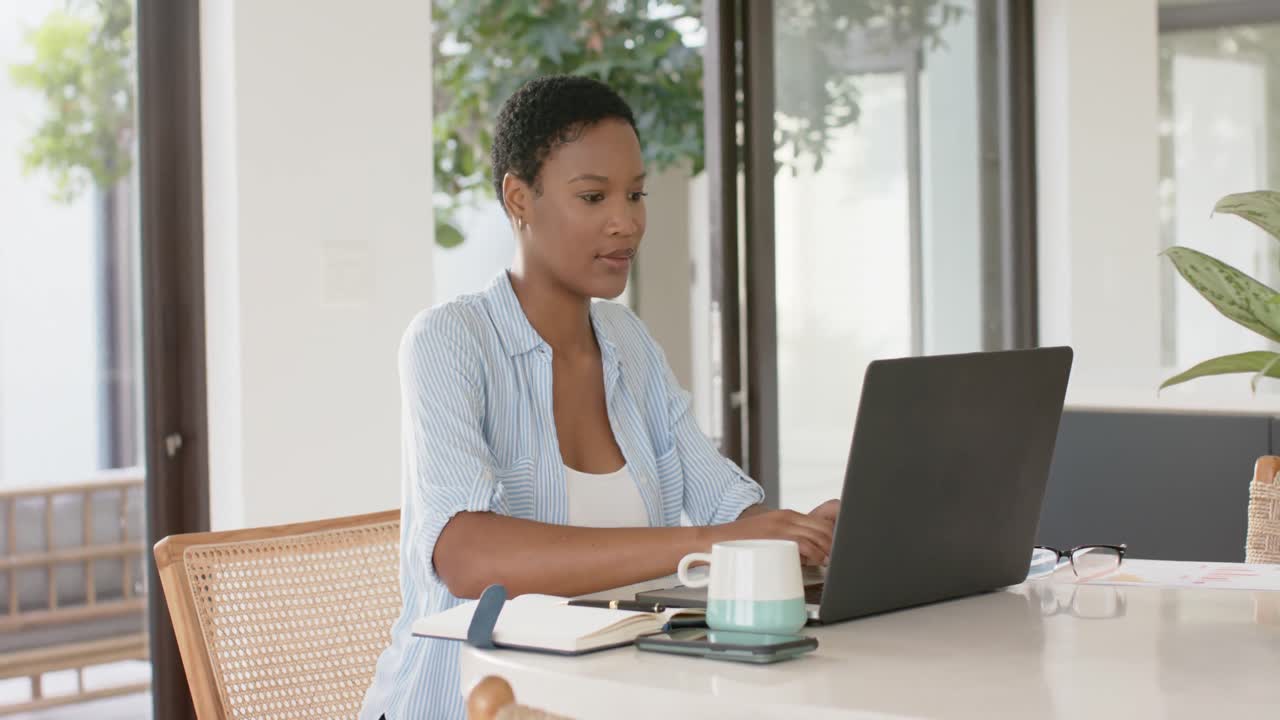mujer afroamericana sentada a la mesa y usando computadora portátil, cámara lenta