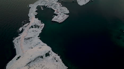 Mountain-peak-aerial-view-overlooking-frozen-Lofoten-small-town-fishing-village-archipelago-islands