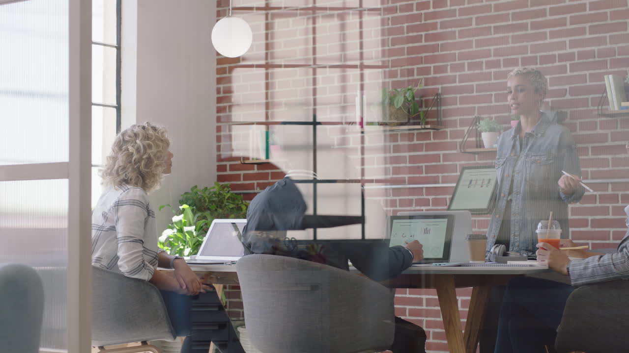 молодая афроамериканская бизнесменка использует цифровой планшетный компьютер, представляя финансовые данные, показывая коллег в офисе презентацию, разнообразную команду, сотрудничающую, стратегию мозгового штурма