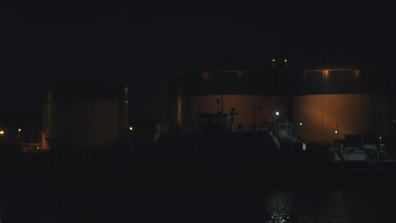 Ripresa in movimento di un'area industriale portuale di notte che riprende edifici, gru e traghetti