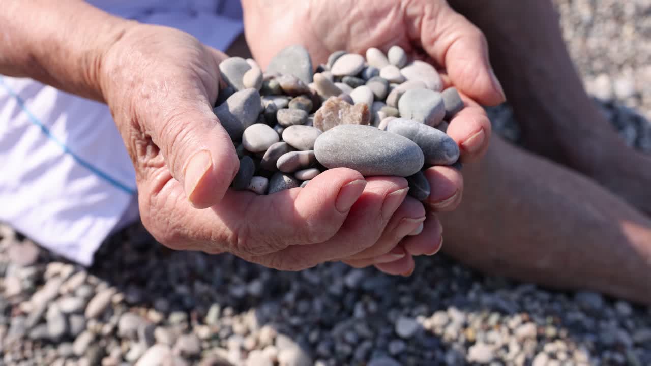 Mani di donne anziane che tengono sassi sulla spiaggia