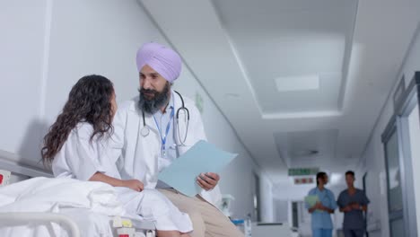 diverse sikh male doctor in turban and child patient talking in corridor at hospital, in slow motion