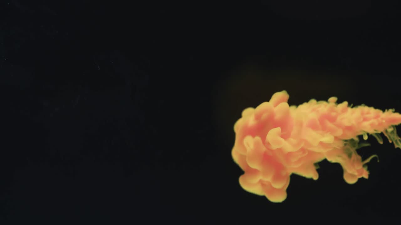 замедленное видео желтого акварельного чернила, смешивающегося с водой на черном фоне