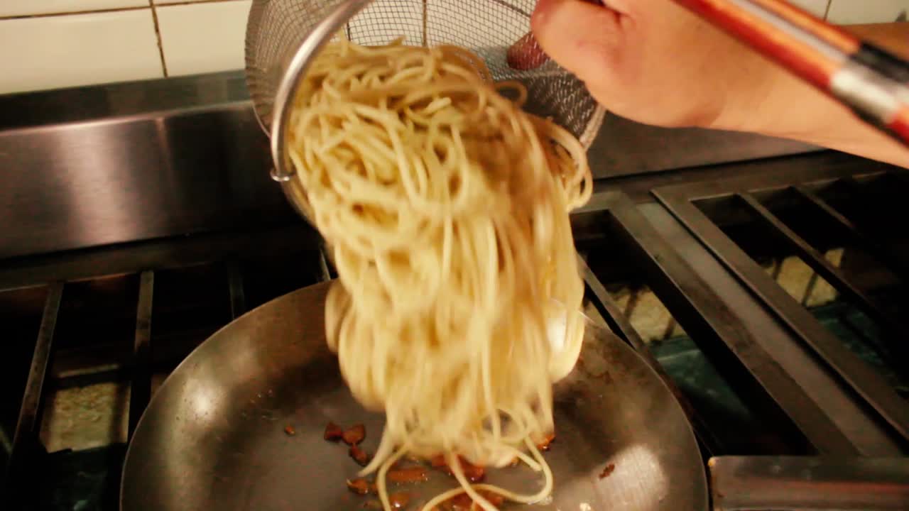 A female chef puts spaghetti on a hot pan, working in restaurant kitchen