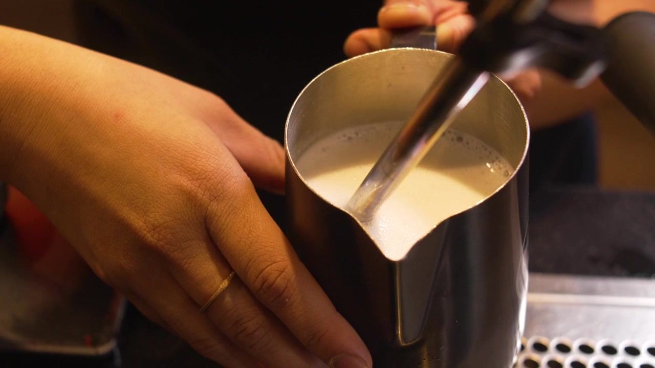 Barista che monta il latte con la lancia vapore per latte macchiato o cappuccino in una caffetteria specializzata