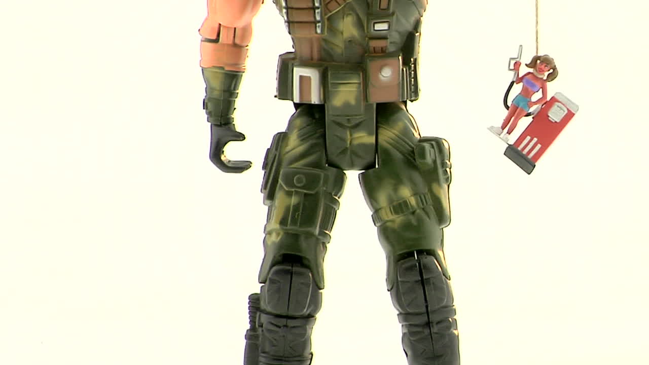 An Army action figure holds a plastic figurine of a woman at a gas pump by a string