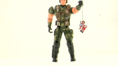 an army action figure holds a plastic figurine of a woman at a gas pump by a string