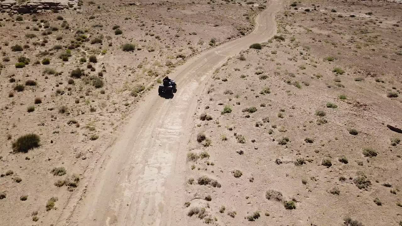 Lonely Man Driving ATV Quad Fourwheeler on Dusty Road in Dry Desert Landscape, Tracking Aerial View, Utah USA