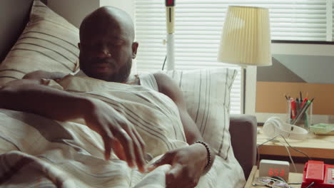 african american man waking up in bed and turning off alarm clock