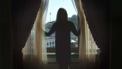 young woman walking to window and opening curtains back view