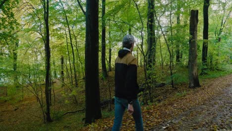 Explorando-A-Un-Tipo-Alto-Con-Gorra-Camina-En-El-Bosque-Otoñal-De-Gyllebo-Y-Da-La-Vuelta,-Österlen-Suecia---Seguimiento-De-Plano-Ancho-A-Medio-Desde-La-Parte-Trasera