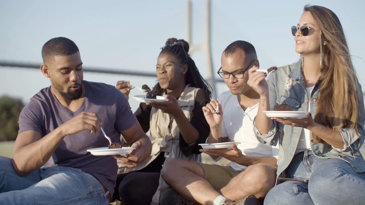 jóvenes amigos alegres comiendo un delicioso pastel en el parque