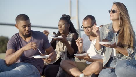 Cheerful-young-friends-eating-delicious-cake-in-park