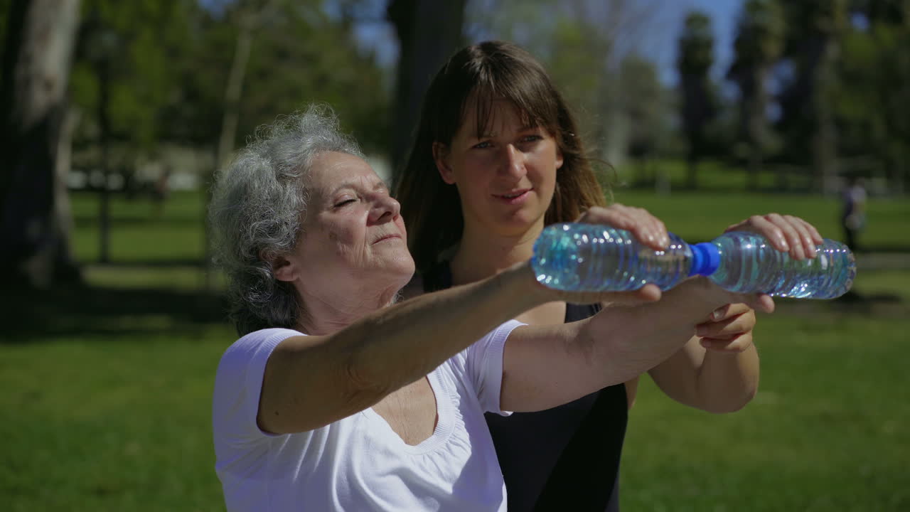 una mujer mayor tranquila entrenando con un entrenador personal alegre en el parque.