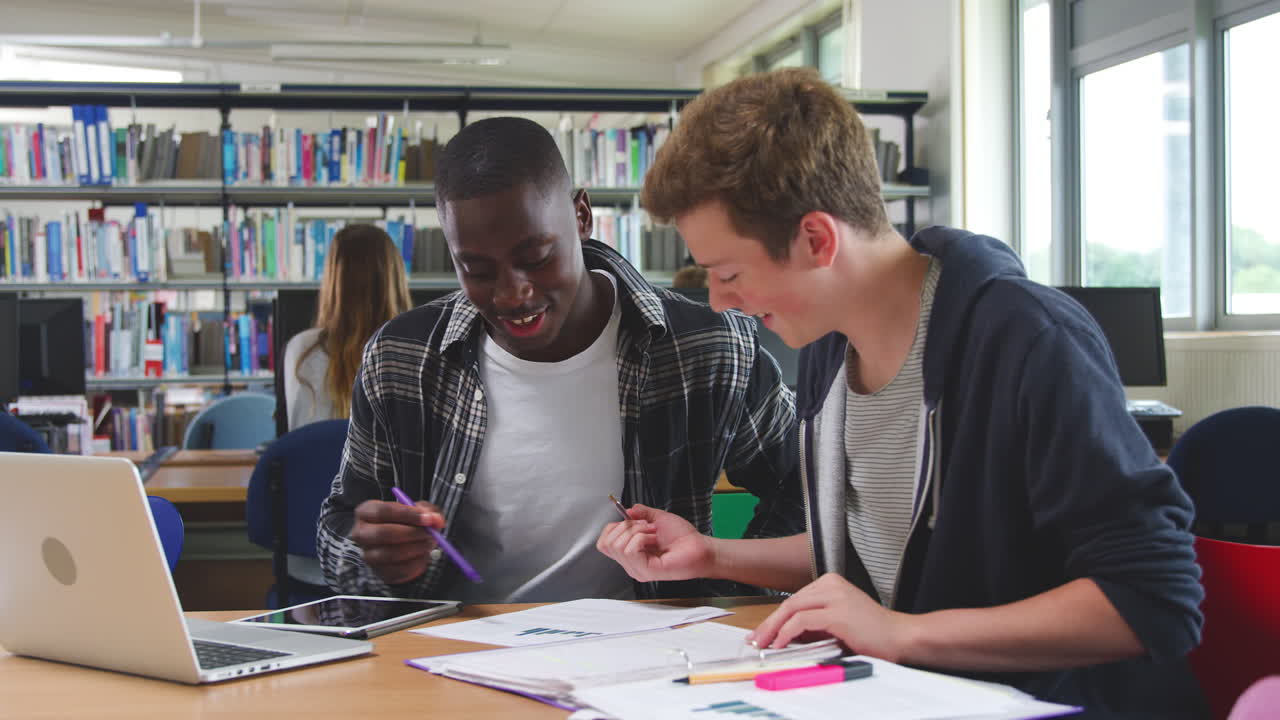 Two Male College Students Working On Laptop Together In Library