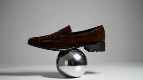 brown loafer balanced on a reflective sphere