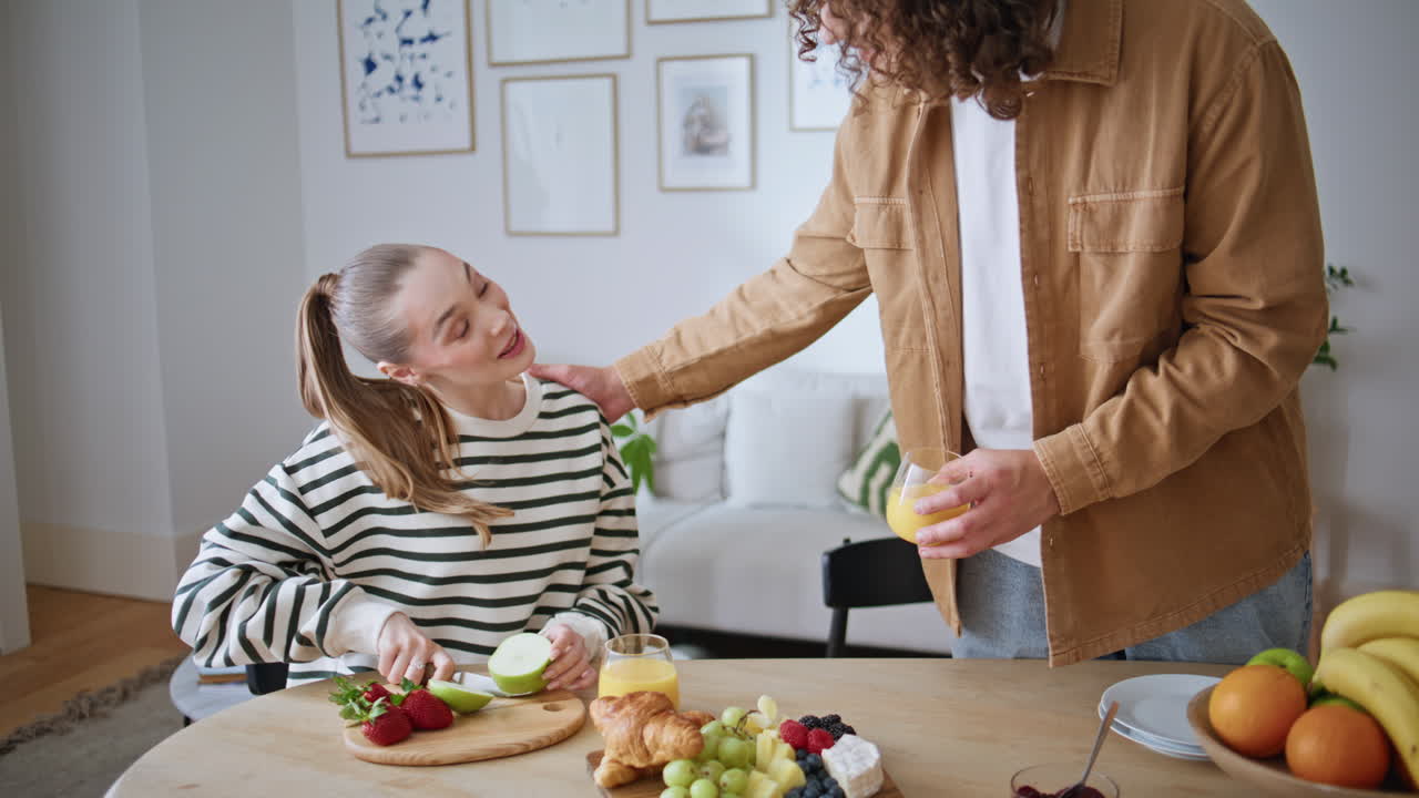 Caring man bringing juice to woman slicing apple for family breakfast closeup