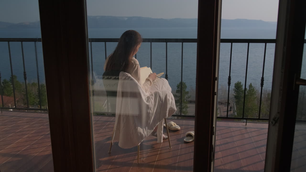 Woman relaxing on a balcony with a lake view, drawing