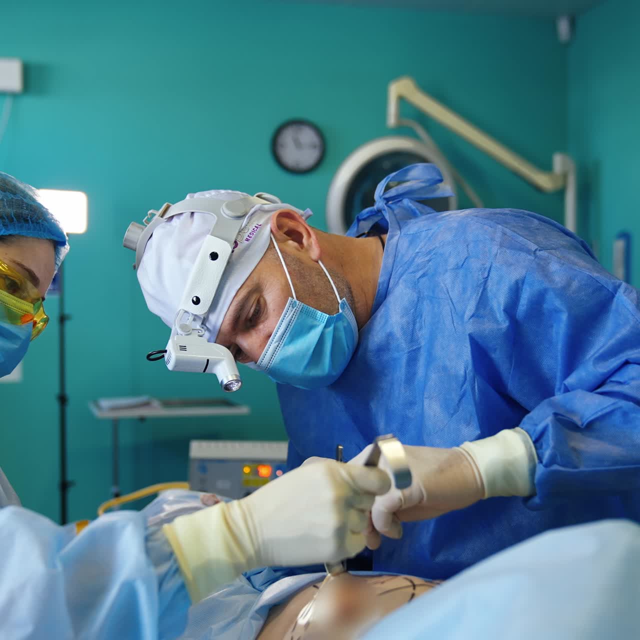 Female nurse hold the lifted skin of a patient with a metal tool. Surgeon applies instruments in the breast cavity preparing place for implant