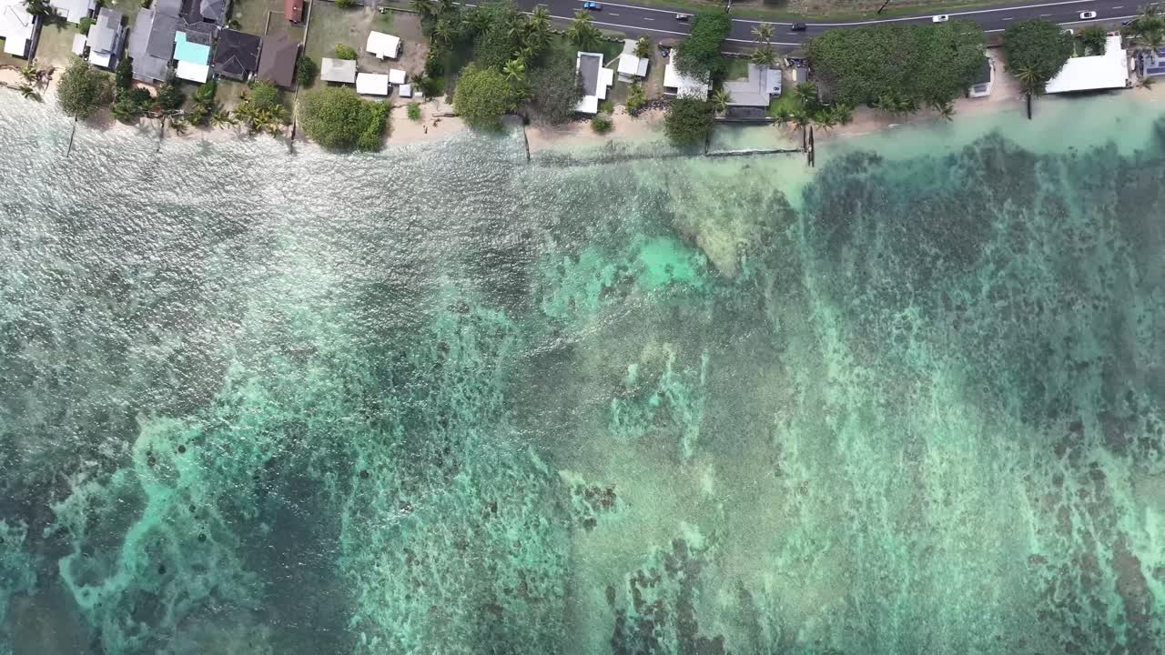 Aerial top-down drone footage of clear blue water on a sandy beach in Oahu, Hawaii, showcasing turquoise water, white surf, tropical coastline, and the rhythmic motion of waves along the shore