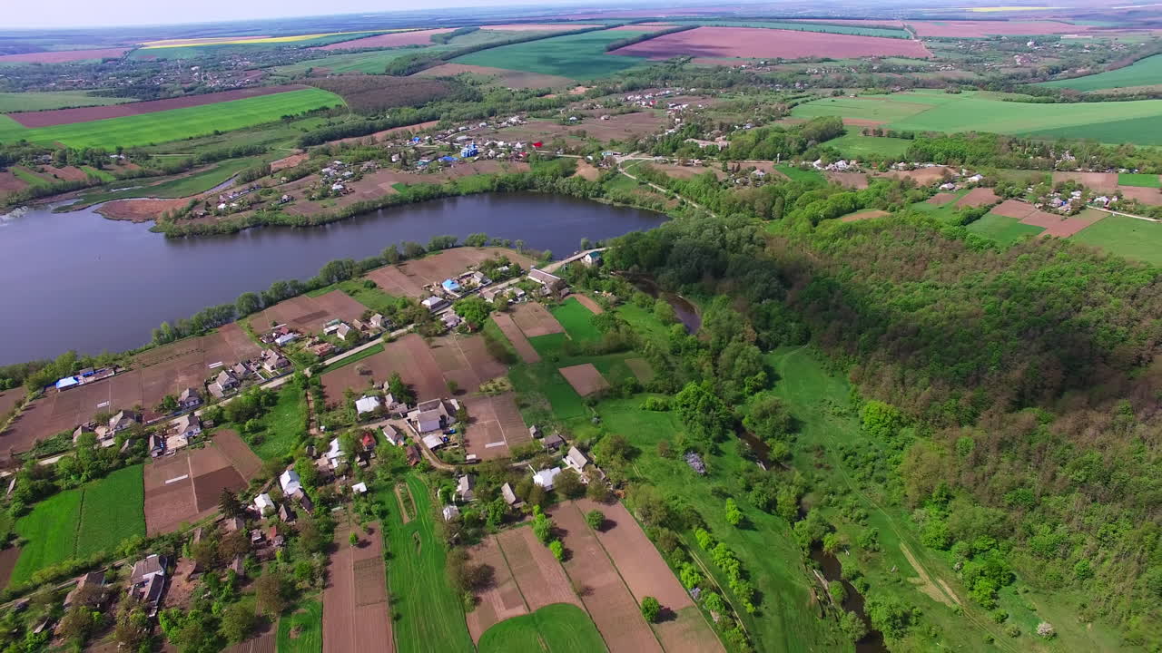 Large village locating at the bank of the river. Agricultural farmlands and green forests surrounding the rural area. Top view.