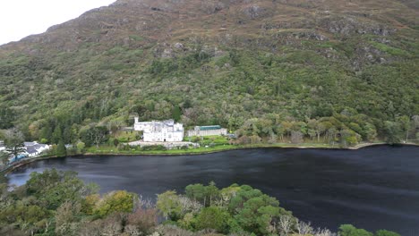 Aerial-dolly-shot-of-the-historic-and-oldest-Benedictine-Abbey-the-Kylemore-Abbey-in-Connemara-Galway,-Ireland-overlooking-a-black-river-which-mirrors-the-abbey-and-a-beautiful-green-landscape