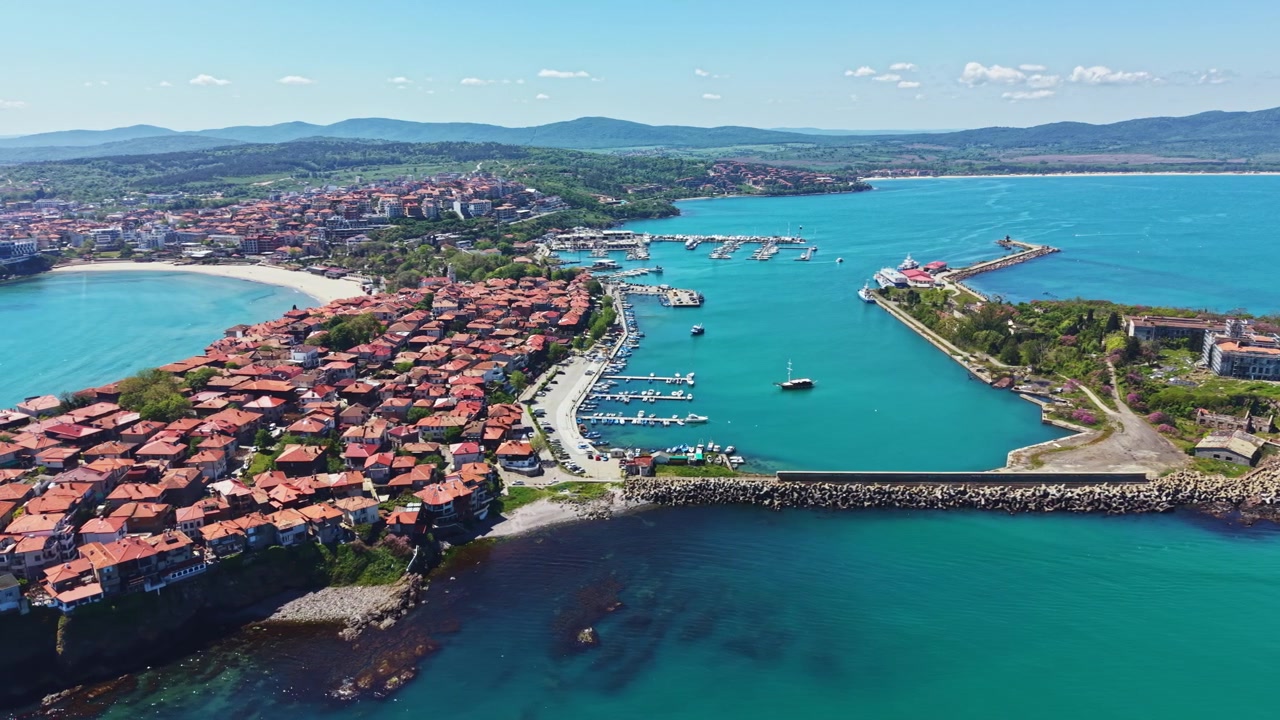 Nessebar manzaraları; limanda tekneler, plaj, açık gökyüzü ve uzakta görünen dağlar ile gündüz çekimi.