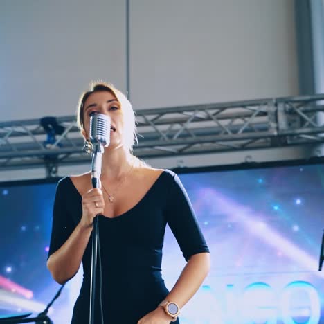 woman singer on the modern scene in the daytime. beautiful female in black dress singing into the microphone on a stage for special event.