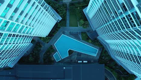 top down flying upwards shot of swimming pool in between two apartment buildings, symmetrical look